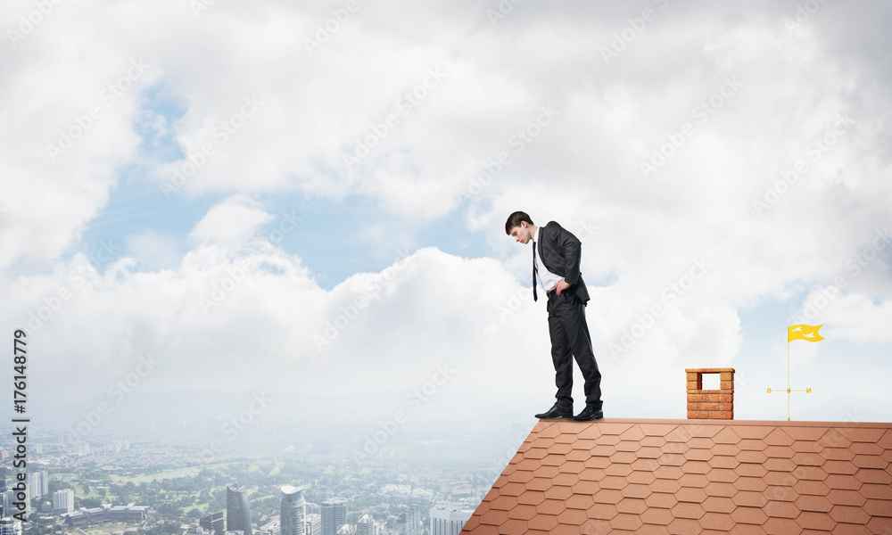 Businessman looking down from roof and afraid to make step. Mixed media Businessman looking down from roof and afraid to make step. Mixed media