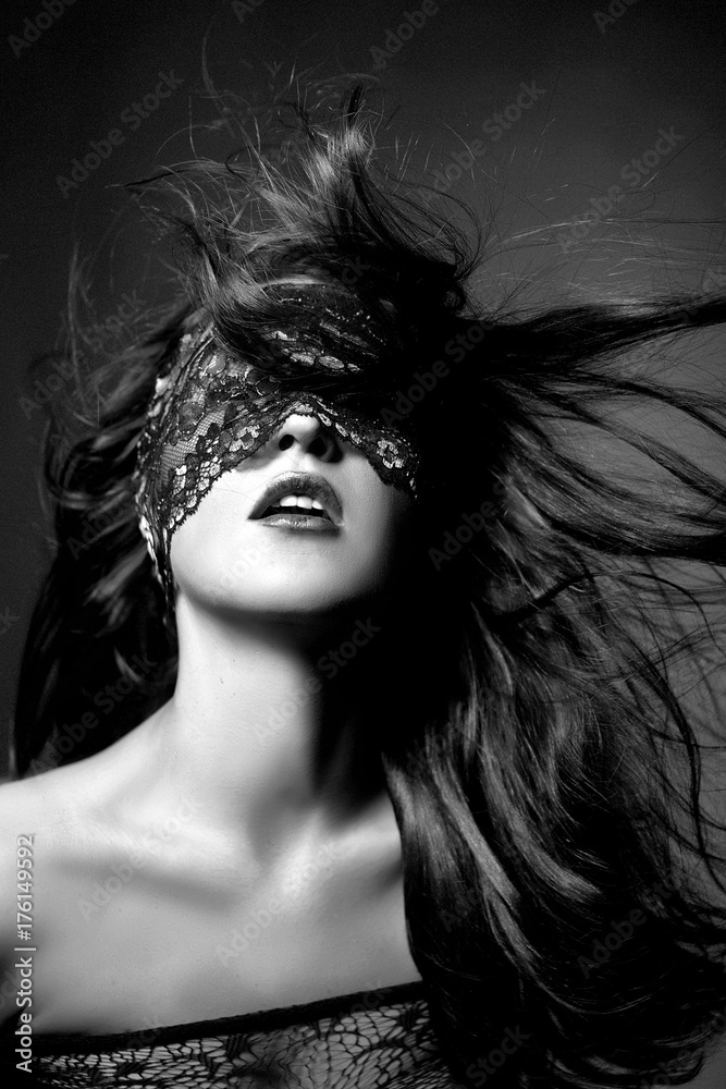Sexy girl in black lingerie on black background. Erotic photoshoot charming attractive woman with a blindfold mask on her face. The girl's hair flying in the air