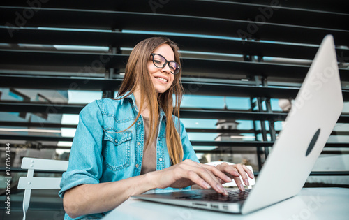 Casual stylish cheerful girl wears jeans scirt works with laptop computer near modern building wall outdoor