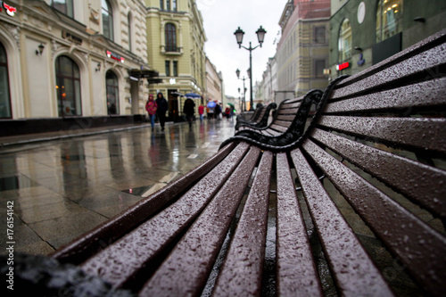 lonely wooden bench in the street in the rain, in the background of a muddy street, evening