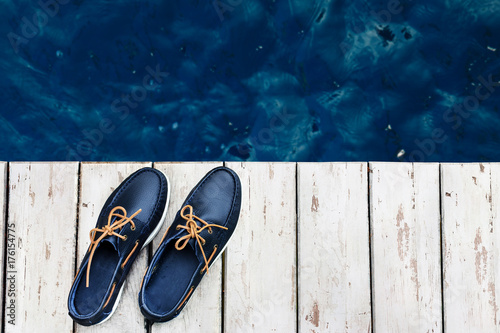 Blue leather men's top sider shoes or boat shoes with white sole on a white wooden pier or on a white wooden boards near the water, or rivers, or lakes, or the sea. Fashion advertising shoes photos.