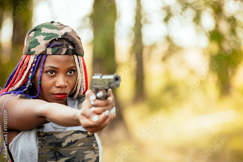 Portrait of a beautiful young African American girl with a dreadna haircut with a gun in her hands. she aims at the attacker. photo self defense concept