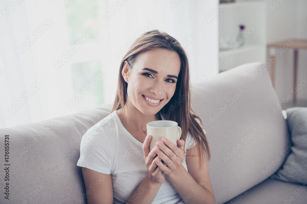Morning is here! Close up portrait of dreamy gorgeous brown haired freelancer on the beige couch at home having hot beverage, looking in camera, so comfortable, with beaming smile Morning is here! Close up portrait of dreamy gorgeous brown haired freelancer on the beige couch at home having hot beverage, looking in camera, so comfortable, with beaming smile