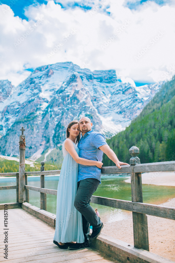 Naklejka premium Man and woman on vacation in beautiful place mountains.Young couple in love on the pier at lake, lago di braies,Dolomite,Italy.