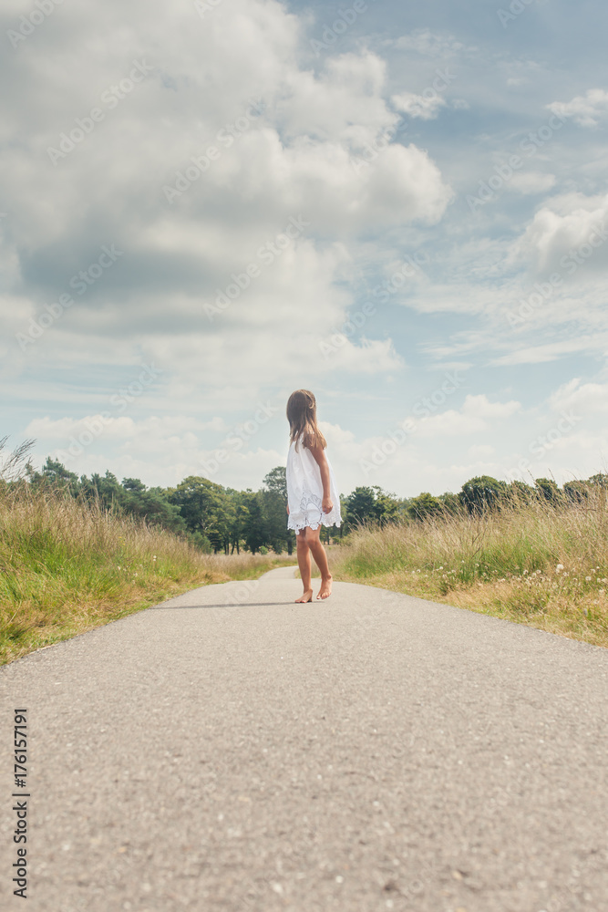 Little girl barefoot in a white dress walking on a long road Stock ...