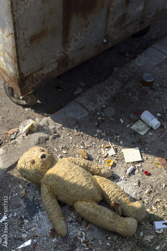 Broken teddy bear next to a dumpster
