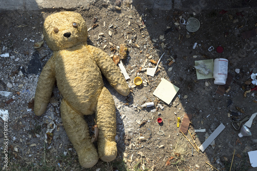 Broken teddy bear next to a dumpster