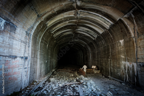 A man standing in a dark train tunnel looking into the darkness