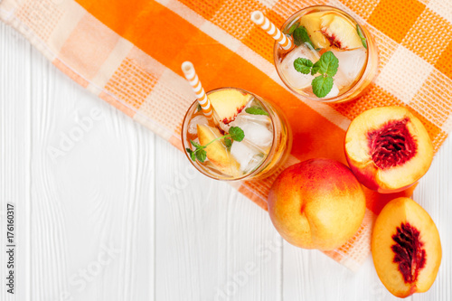 Peach lemonade with ice and mint leaves. Homemade lemonade of ripe nectarine with white and orange ripe. Two glasses of peach tea. Refreshing summer drink on a white wooden background.
