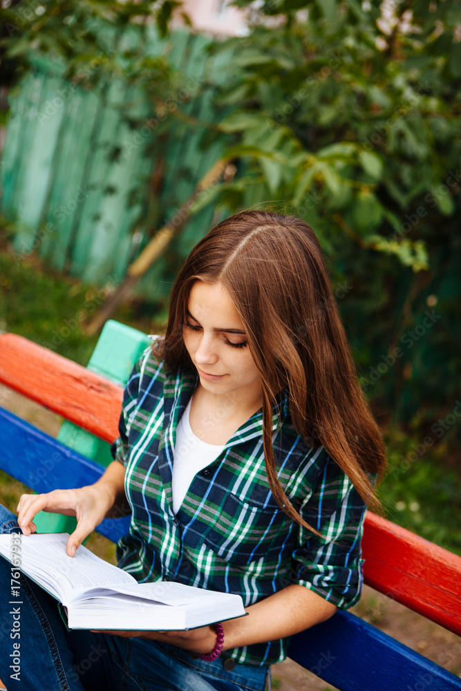 Obraz premium Beautiful girl reading book outdoors, with copy space