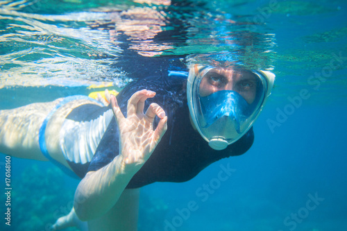 Snorkel girl underwater shows ok gesture. Snorkeling in full face mask.