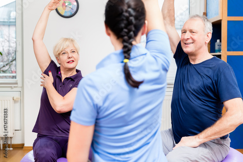 Elderly woman and man doing exercises with physiotherapist on gymnastic balls