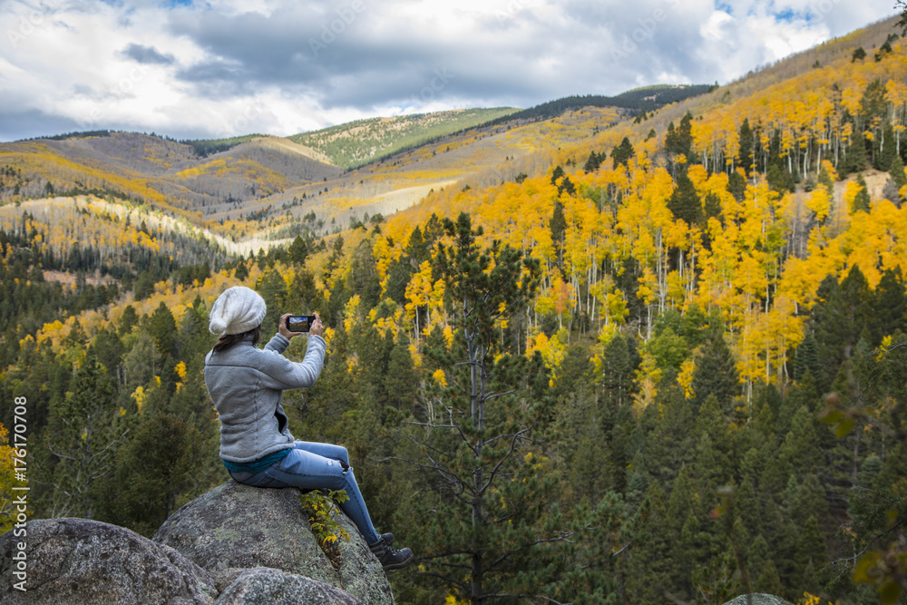 Naklejka premium woman taking picture with cell phone of beautiful mountains covered in fall colors