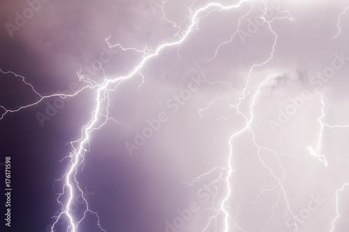 Thunder storm lightning strike on the dark purple cloudy sky background at night