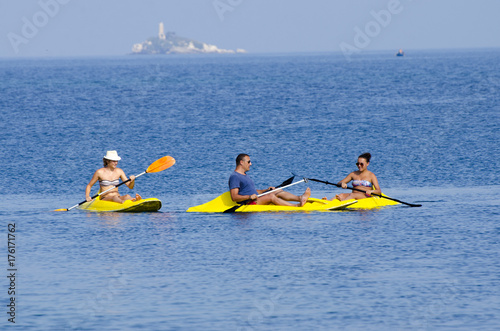 Young people are kayaking on a sea in beautiful nature with island at background. Summer sunny day in outdoor