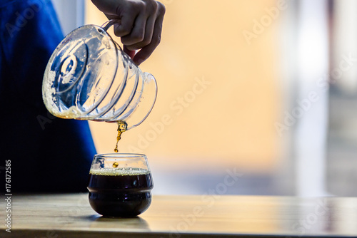 Professional barista spills fresh brewed pour-over made of the best Arabica roasted beans. The process of coffee brewing in the cozy morning atmosphere of a coffee shop. 
