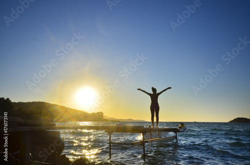 Happy woman standing arms outstretched back and enjoy life on the beach pier at Sea sunset