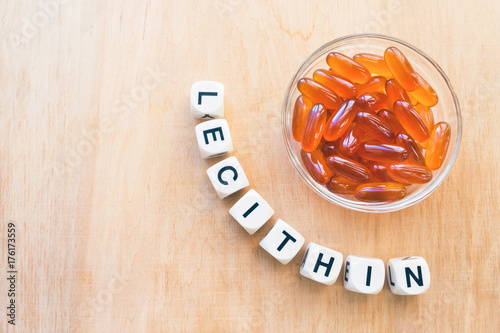 Lecithin gel pills in a round glass bowl and with the word Lecetin from the letters of cubes on a light wooden background. Soy and sunflower lecithin benefits for skin, digestion, lower cholesterol. photo