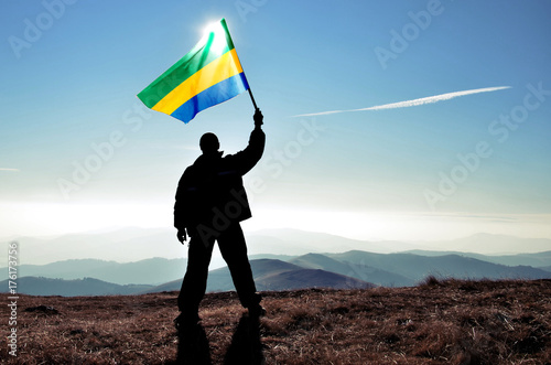 Successful silhouette man winner waving Gabon flag on top of the mountain peak photo