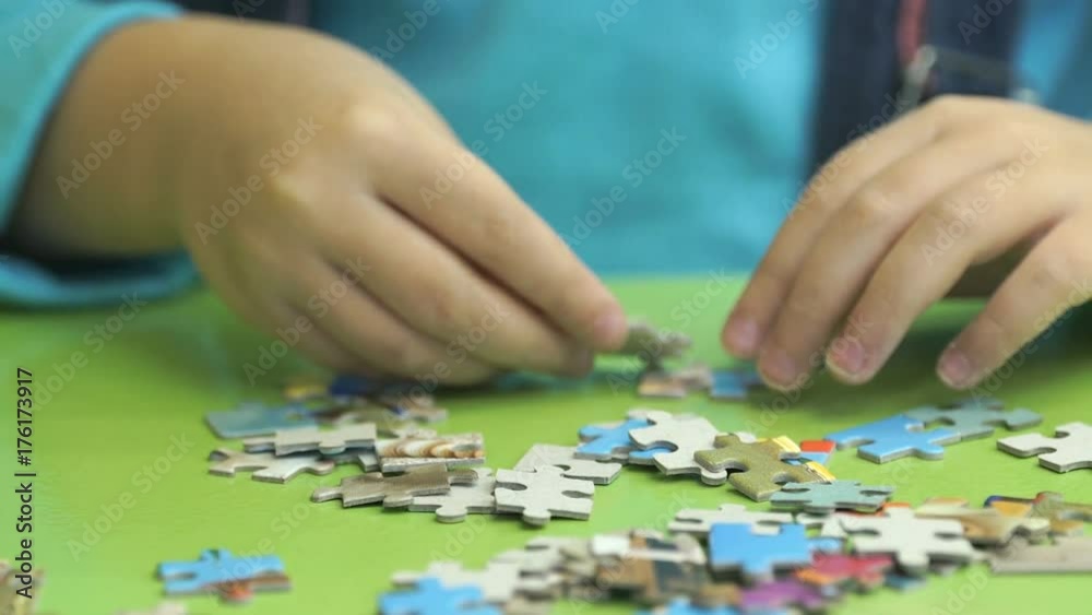Close-up of hands of little unidentified child collecting picture from puzzles at the table in kindergarten Close-up of hands of little unidentified child collecting picture from puzzles at the table in kindergarten