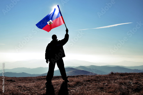 Obraz na plátně Successful silhouette man winner waving Haiti flag on top of the mountain peak