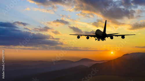 Plane taking off over mountain range at sunset