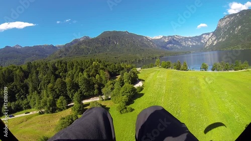 POV, CLOSE UP: Paraglider flying close above ground before landing on meadow field. Unrecognizable person paragliding above scenic rural countryside with vast pasture fields, rocky mountains and lake