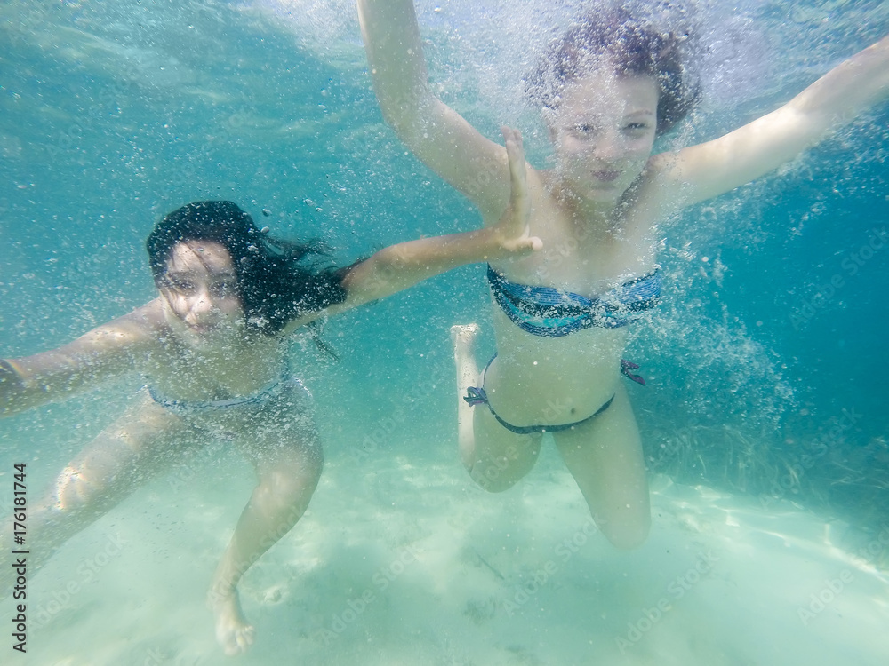 Two girls having fun swimming underwater in turguise sea water smiling. Selfie in ocean