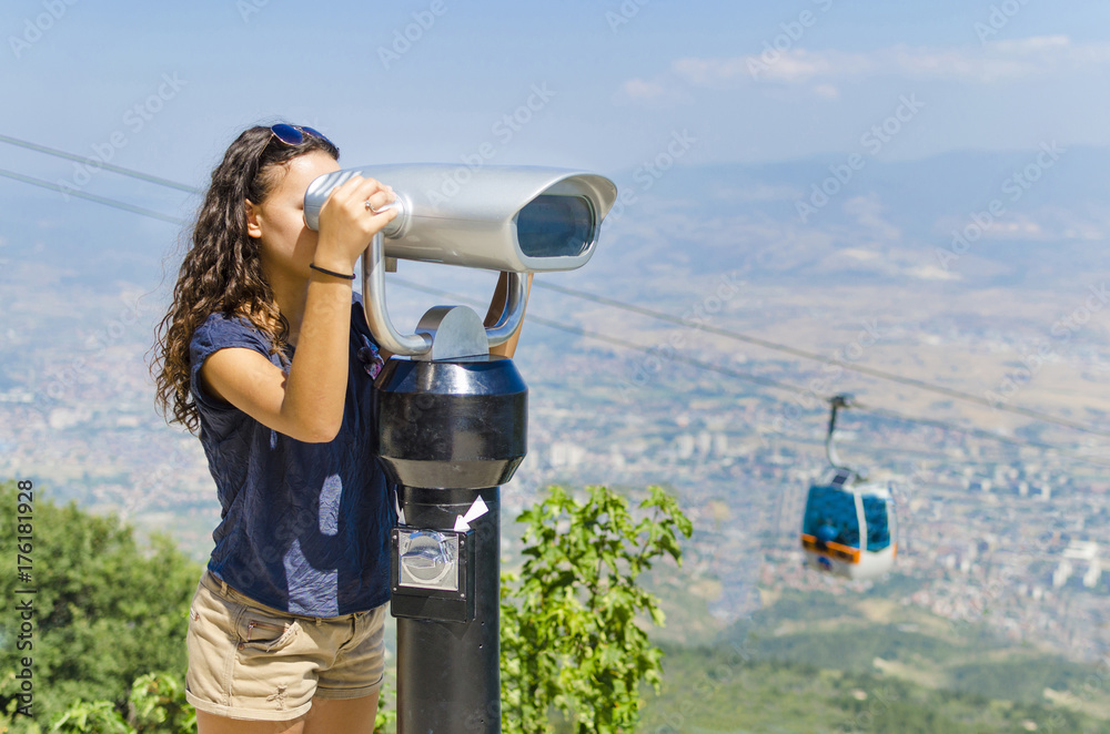 Beautiful curly hair teenage girl using coin binocular viewing the Skopje cityscae from Vodno mountain in Macedonia