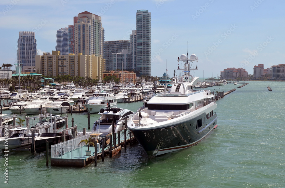 Mega luxurious motor yacht docked at a marina in Miami Beach with luxury high-rise condominiums over looking the marina and the Atlantic Ocean in the background.