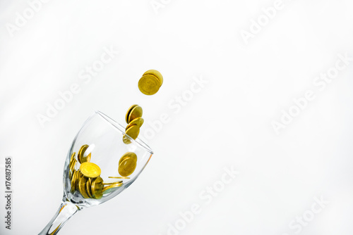 Golden coins splash in a glass of champagne on the wall background with copy space. © pookpiik