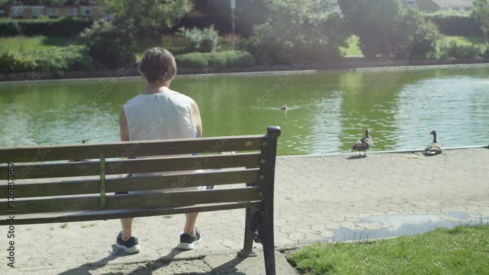 Senior man takes a break from exercising in the park & looks out over lake Senior man takes a break from exercising in the park & looks out over lake