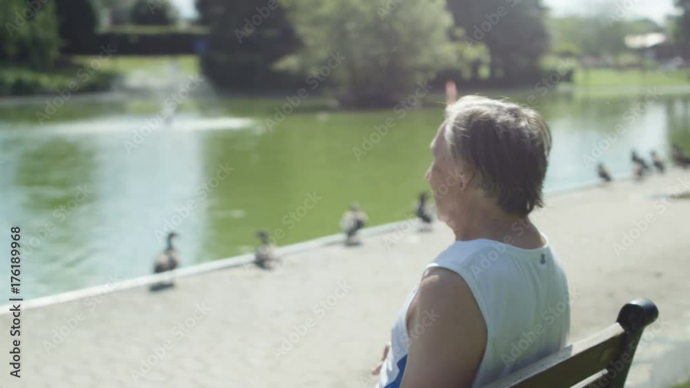  Senior man takes a break from exercising in the park & looks out over lake