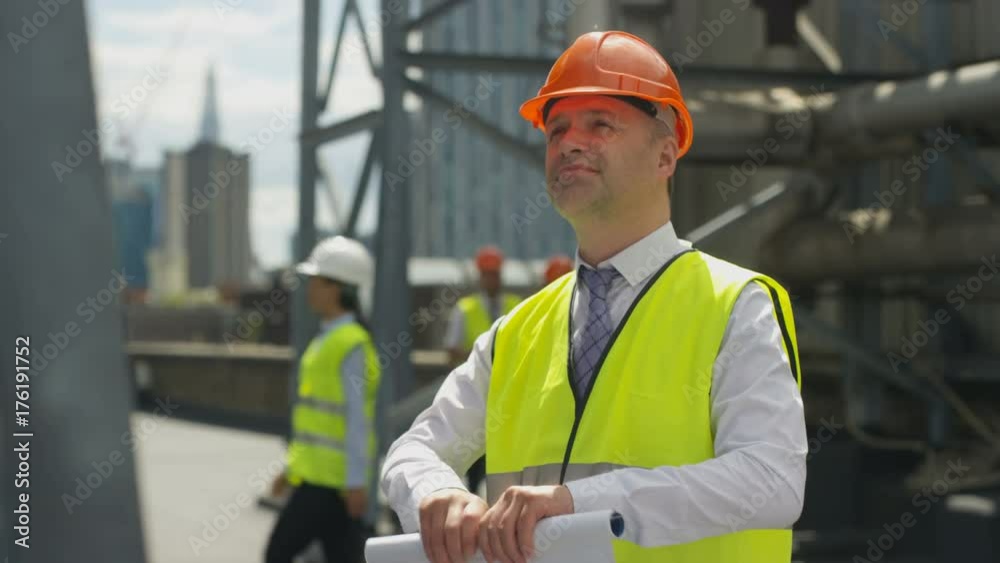 Portrait smiling engineer on site with colleagues working in background Portrait smiling engineer on site with colleagues working in background