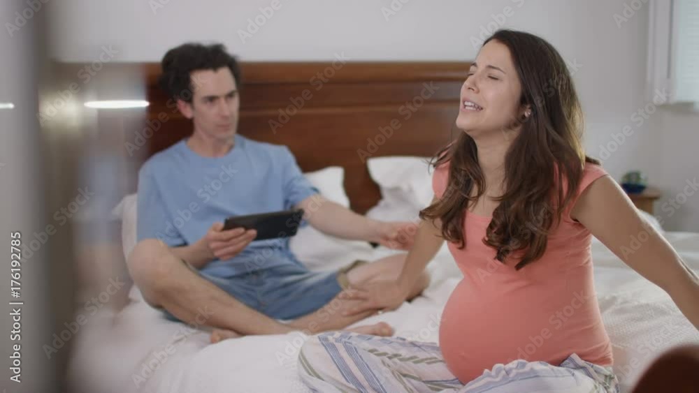 Couple expecting a baby together in bed, woman starting contractions Couple expecting a baby together in bed, woman starting contractions