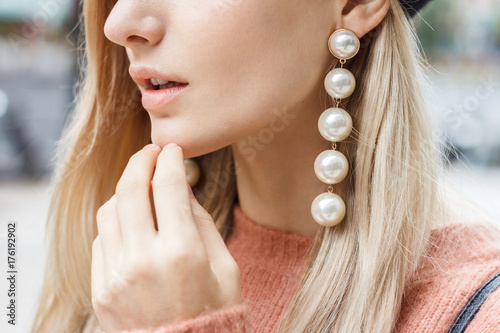Close up detail of beautiful young blonde woman dressed in pink sweater with gorgeous earrings made of big pearls. 