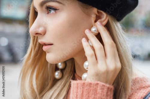 Close up detail of beautiful young blonde woman dressed in pink sweater with gorgeous earrings made of big pearls. 