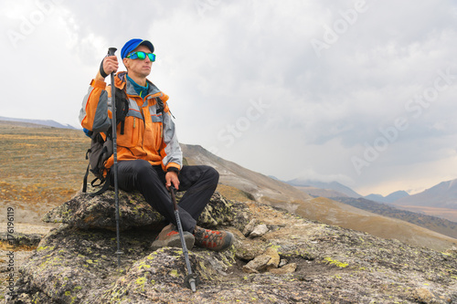 A lonely tourist with a backpack and in sunglasses is resting sitting on a rock