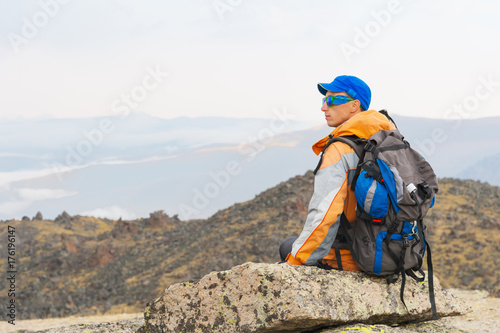 A lonely tourist with a backpack and in sunglasses is resting sitting on a rock