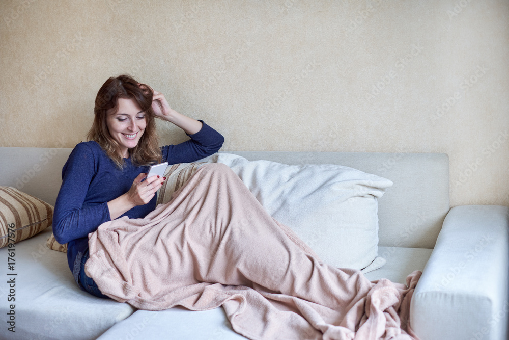 Young women using her smart phone on couch at home in the living room Young women using her smart phone on couch at home in the living room