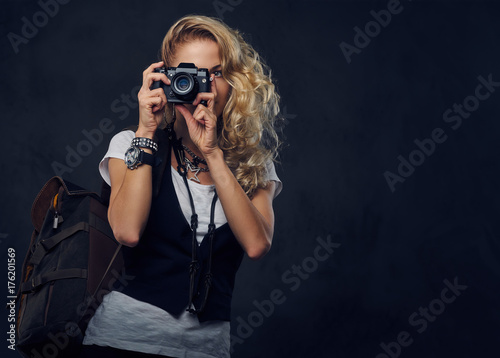Blonde female backpacker holds a compact digital camera.
