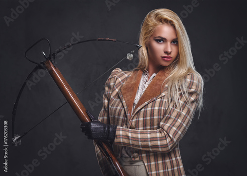 Studio portrait of blond old fashioned female holds a crossbow.