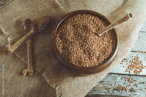 Buckwheat in a wooden bowl and a spoon full of buckwheat on the wooden background