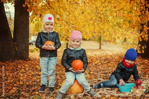 Three happy friends kids in autumn park with small pumpkins.