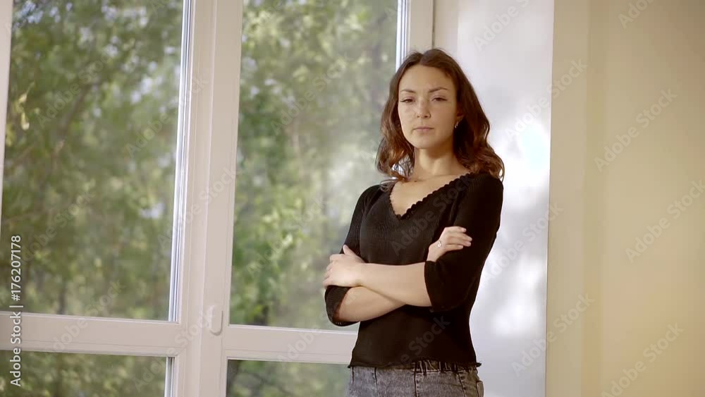 lonely sad woman is standing arms crossed near huge window, looking at a camera, lowering her eyes lonely sad woman is standing arms crossed near huge window, looking at a camera, lowering her eyes