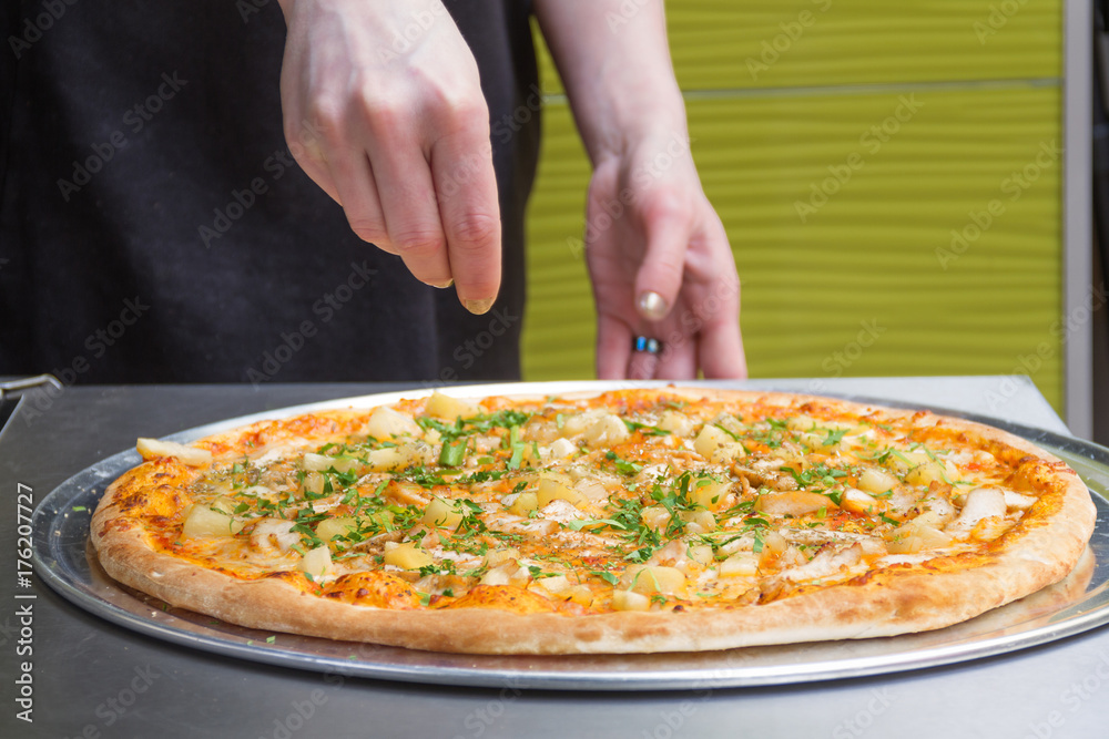 Female hands spread ingredients on pizza