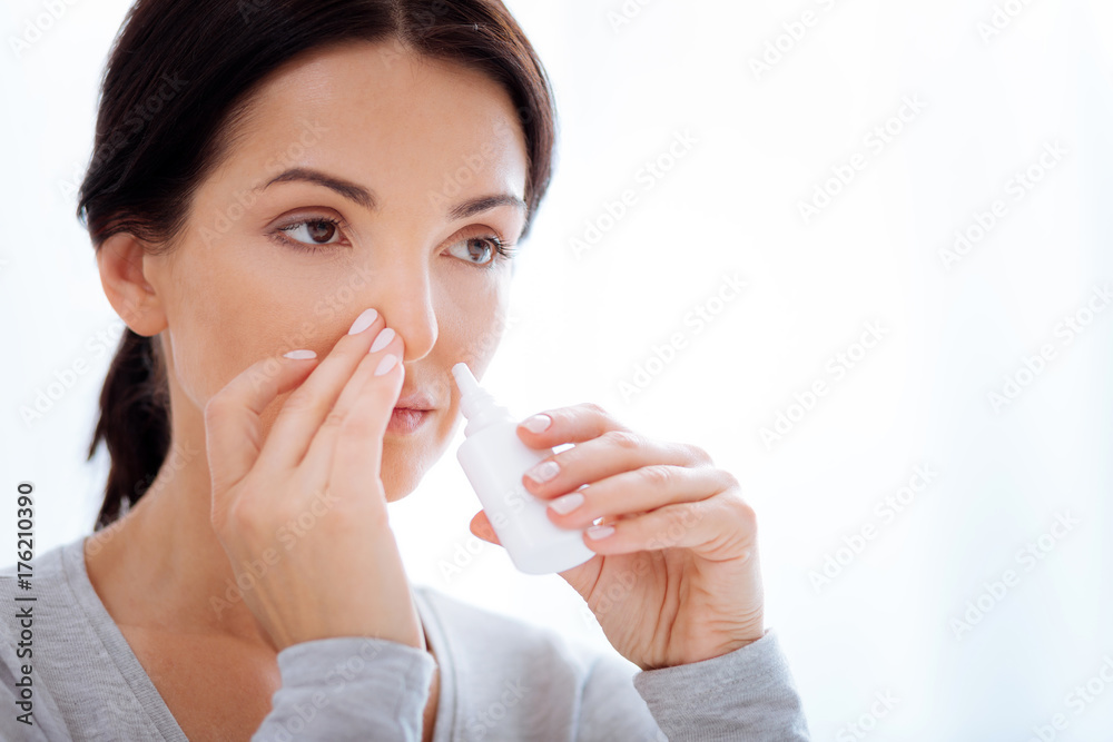 Attentive woman using special nasal drops Attentive woman using special nasal drops
