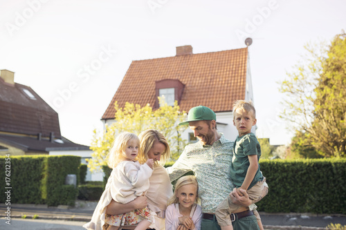 Family with children (18- 23 months, 4-5, 8-9 ) standing in in front of suburban house photo