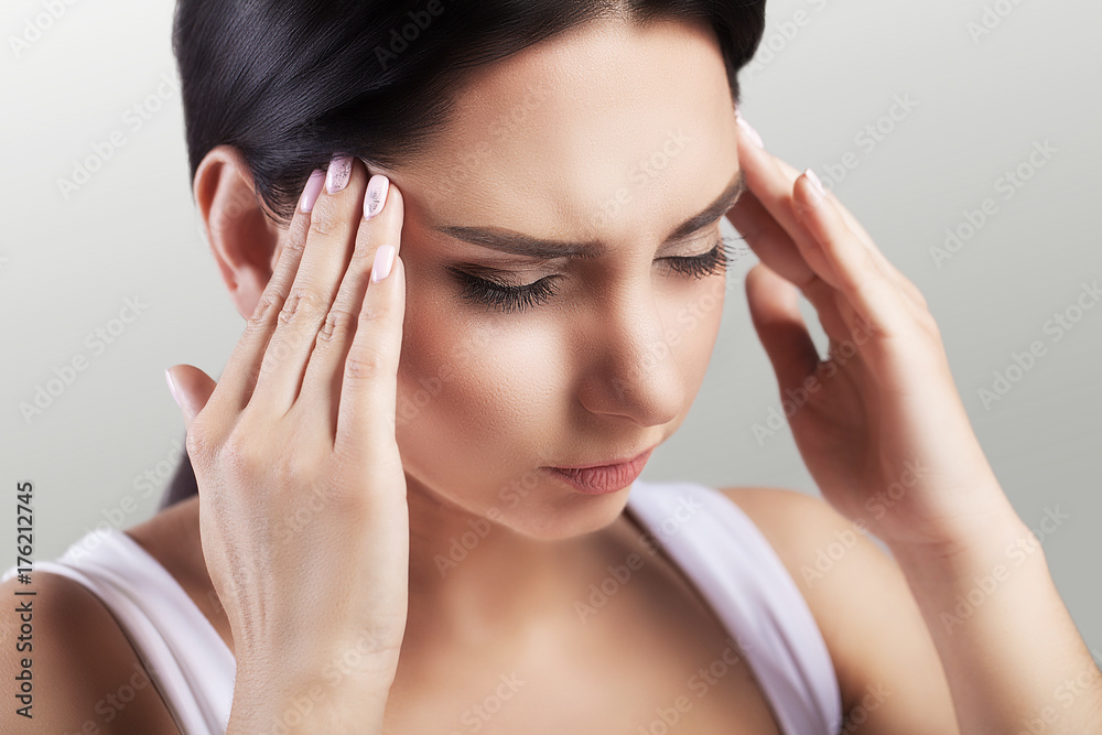 Headache in a young girl. Migraine. Fatigue after a hard working day. The concept of health. On a gray background. Headache in a young girl. Migraine. Fatigue after a hard working day. The concept of health. On a gray background.