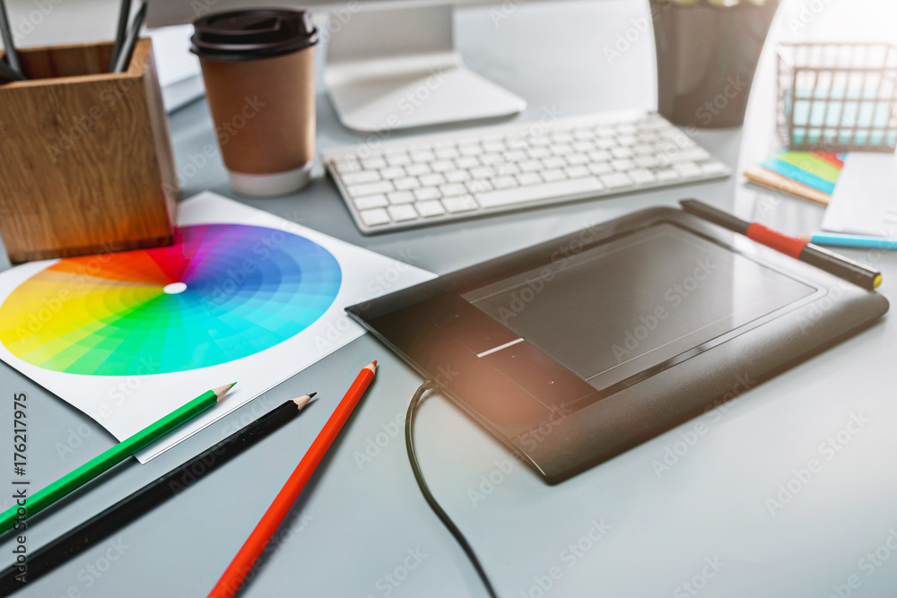 The gray desk with laptop, notepad with blank sheet, pot of flower, stylus and tablet for retouching The gray desk with laptop, notepad with blank sheet, pot of flower, stylus and tablet for retouching